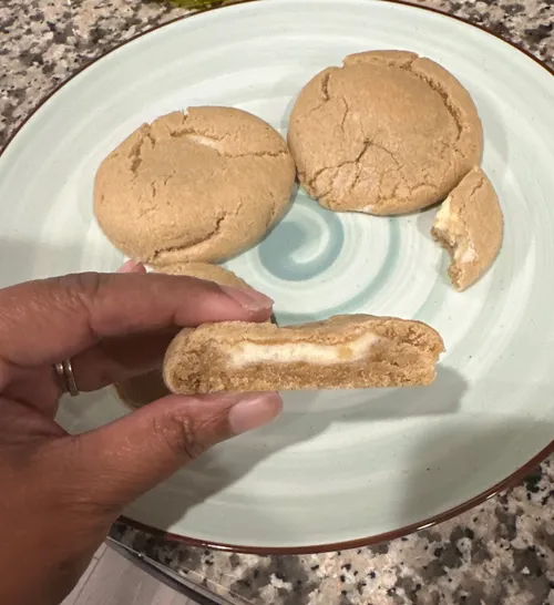Finished butterbeer stuffed cookies on a plate, one broken open to show the cream filling inside